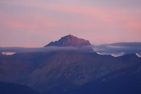 Montagne au crépuscule, ciel rose et violet, nuages accrochés aux crêtes.